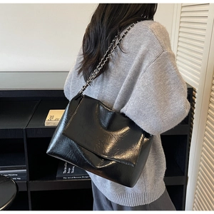 Detail of a chic black textured shoulder bag with metal chain strap on a model