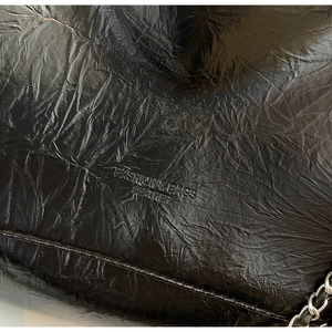Detailed close-up of oily waxed leather texture and embossed logo on the black tote bag