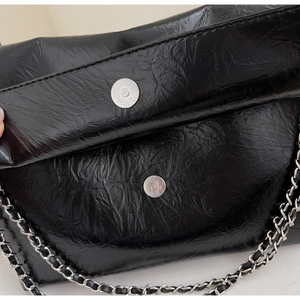 Close-up of black glossy wrinkled leather texture and silver magnetic clasp on tote bag