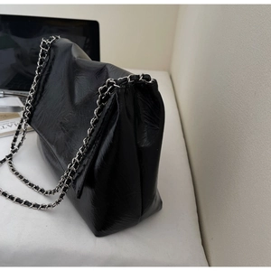 Detail of black glossy wrinkled leather shoulder bag with silver chain strap on a desk