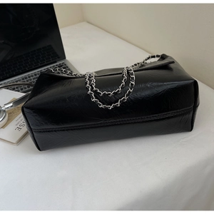 Detail of large black oil-wax leather tote with silver chain strap on an office desk