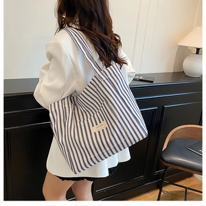 Close-up of a blue striped canvas tote bag worn by a model in a cozy indoor setting