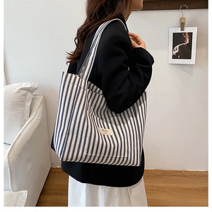 Detail of blue and white striped canvas tote bag with woven label on model's shoulder