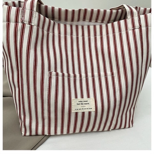 Detail of red and white striped canvas tote bag featuring an outer pocket with fabric label