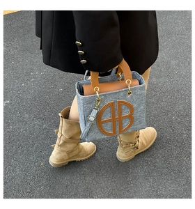 Détail du sac cabas en feutre gris avec anses en cuir marron et logo BB en métal rond