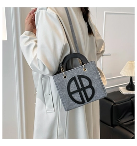 Mannequin portant un cabas en feutre gris avec logo AB en cuir noir et bandoulière