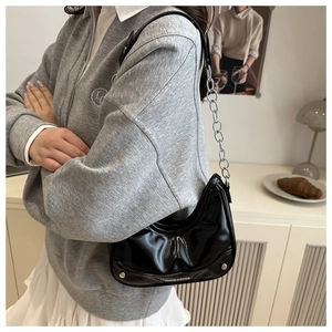 Detailed view of a black patent leather crescent bag with chain strap worn on the shoulder