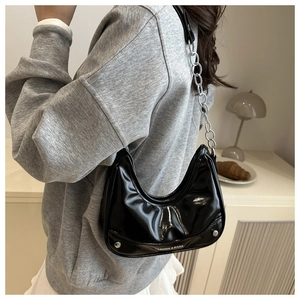 Detail of black patent leather crescent bag with silver rivets and chunky chain strap