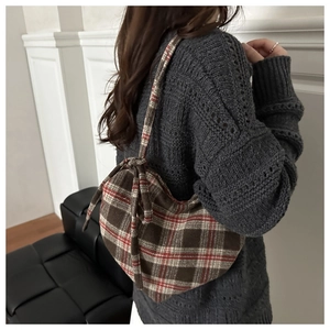 Detail of tartan pattern shoulder bag with ribbon bow and soft tweed texture on a model