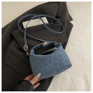 Blaue Handtasche mit Leopardenmuster, Goldbeschlägen und Riemen auf grauem Blazer