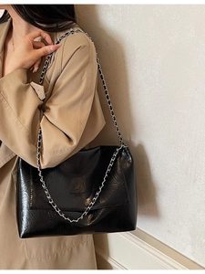 Black glossy leather tote with silver chain strap shown on a model in beige trench coat