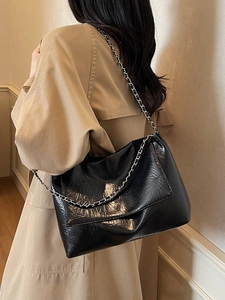 Minimalist black glossy chain shoulder bag for women worn over a beige trench coat