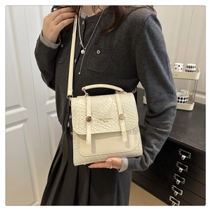 Detail of white woven PU leather handbag with gold studs and top handle on a model