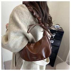 Detail of a brown glossy leather hobo bag with pleated shoulder strap and knotted accents