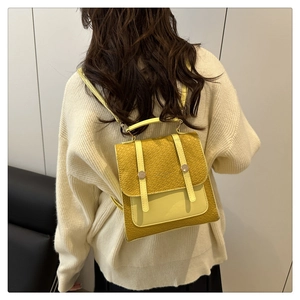 Detail of yellow embossed leather backpack with metal buckles on white knit sweater