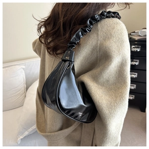 Detail of black glossy faux leather underarm bag featuring a ruched scrunchie shoulder strap
