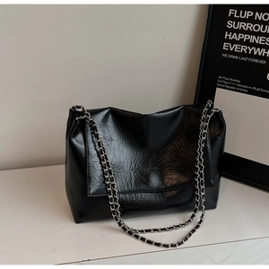 Detail of black leather tote bag with silver chain straps on marble surface