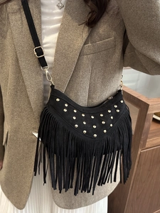 Elegant black fringe crossbody bag with gold rivets shown in a stylish everyday outfit