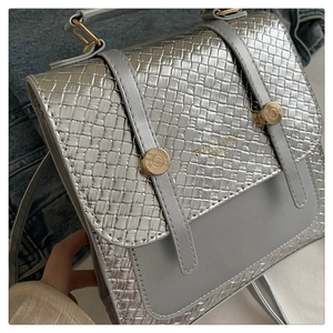 Détail d'un sac à main argenté en cuir synthétique tressé avec boucles en métal doré