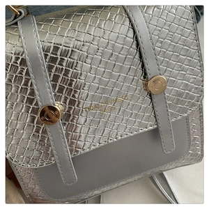 Détail du sac bandoulière argenté avec texture tressée et accents métalliques dorés