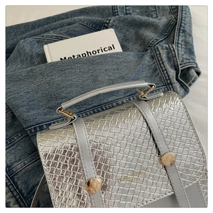 Détail d'un sac bandoulière argenté métallisé avec texture tressée sur veste denim