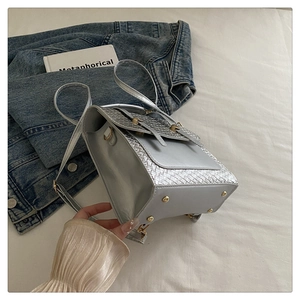 Détail du sac bandoulière argenté avec rabat tressé et clous de protection dorés