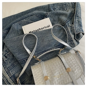 Vue détaillée du mini sac argenté tressé posé sur un denim bleu et un livre blanc