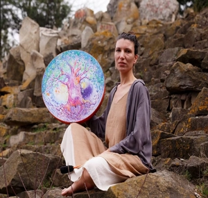 Artistic Tree of Life shamanic drum held by a woman in a natural outdoor rock setting