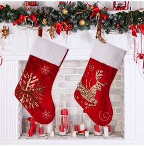 Luxurious red velvet Christmas stockings with gold sequined reindeer and snowflake on fireplace