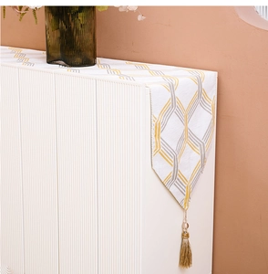 Detail view of white table runner with gold and grey geometric patterns and gold tassels