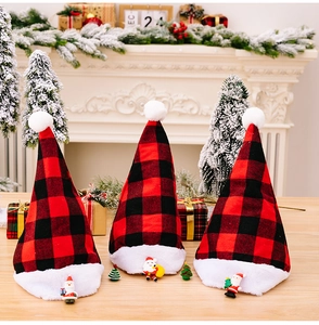 Close-up of three buffalo plaid Christmas hats with plush trim and Santa dolls on wood