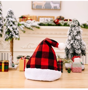 Detail of red and black buffalo plaid Christmas hat with white plush pom on wood surface