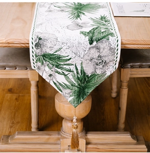 Detail of Christmas table runner with green leaf pattern and golden tassel on wood table