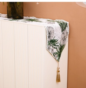 Detail of white table runner with green ink floral pattern and golden tassel pendant