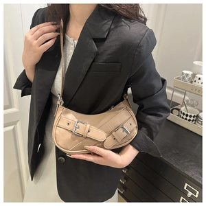 Detail of beige crescent baguette bag with metal buckles on model wearing black blazer
