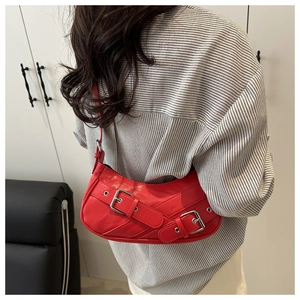 Detail of red leather baguette bag featuring metallic eyelets and rocker style buckle straps
