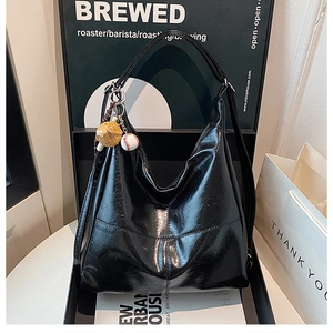 Detail of glossy black tote bag featuring crinkled patent leather and baseball charm