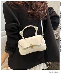 Detail of a beige crossbody bag with a gold buckle and knotted handle on a black blazer