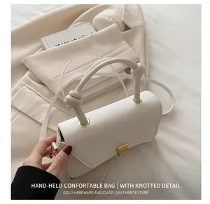 Detail of white structured crossbody bag with knotted handle and gold metal hardware