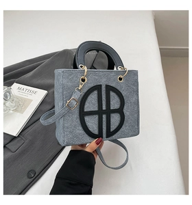 Détail du sac à main en feutre gris avec logo en cuir noir et boucles métalliques dorées