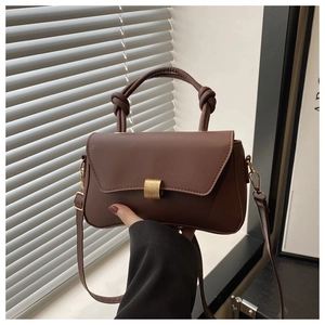 Detail of dark brown leather handbag with gold square buckle and thick knotted handle design