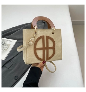 Détail du sac cabas en toile montrant le logo AB en cuir marron et les ferrures dorées