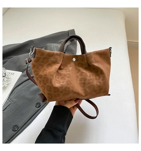 Detail of leopard print suede handbag featuring brown handles and magnetic buckle closure