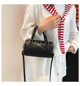 Close-up of heart-quilted black cylinder bag with silver bow hardware on a model