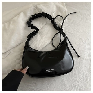 Detail of glossy black crescent bag featuring pleated handle and bow knot decoration
