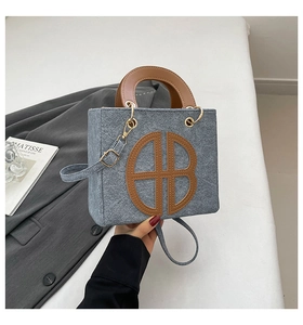 Détail du sac bandoulière en denim bleu avec poignée en cuir marron et boucles dorées