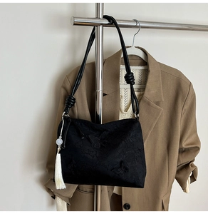 Detail of black tote bag with butterfly pattern, white tassel and knotted shoulder strap