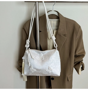 Detail of white satin shoulder bag with floral embroidery, butterfly accents and tassel