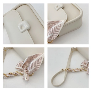 Détail du sac à bandoulière blanc cassé avec chaîne dorée et accessoire foulard en soie