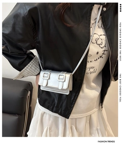 Close-up of a mini silver metallic crossbody bag with double rectangular buckle detail